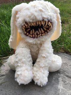 a white stuffed animal with teeth and fangs on it's face sitting in the grass