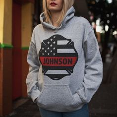 a blonde woman wearing a grey sweatshirt with the american flag on it, standing in front of a building