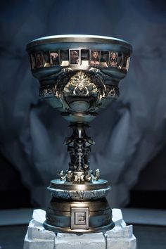 an ornately decorated silver and gold cup on a marble pedestal with a black background