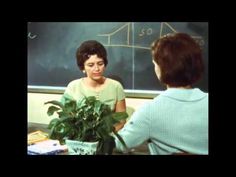 a woman is talking to another woman in front of a blackboard with a plant