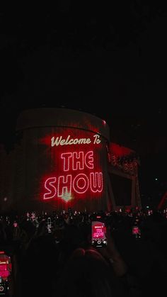 people are taking pictures with their cell phones in front of the show sign at night