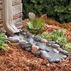 a garden with rocks and plants in the ground next to a brick wall that has a water feature on it