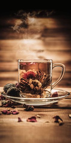 a glass cup filled with lots of tea sitting on top of a saucer next to dried flowers