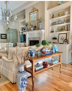 a living room filled with furniture and a fire place under a chandelier on top of a hard wood floor