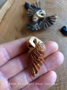 a hand holding a small owl figurine on top of a wooden table next to another bird