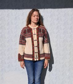 a woman standing in front of a white wall wearing jeans and a cardigan sweater