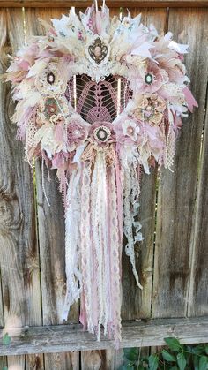 a pink and white wreath hanging on the side of a wooden fence next to a plant