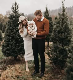 a man holding a baby in his arms while standing between two rows of christmas trees