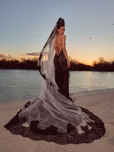 a woman in a wedding dress standing on the beach at sunset with her veil blowing in the wind