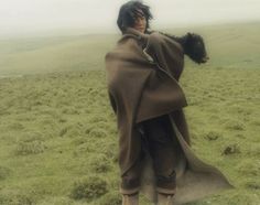 a woman in a brown cape standing on top of a lush green field