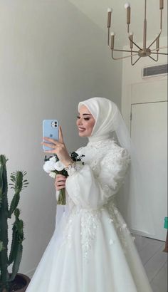 a woman in a wedding dress taking a selfie with her cell phone while holding a flower