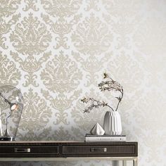 two vases with flowers on a table in front of a wallpapered background