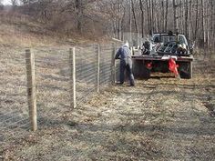 two men working on a fenced in area with a truck behind them and trees