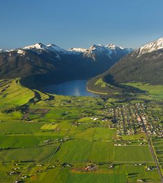 an aerial view of a town surrounded by green fields and mountains with snow on top