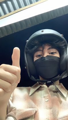 a man wearing a helmet gives the thumbs up sign with his right hand as he wears a black face mask