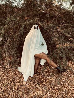 a woman dressed up as a ghost sitting in the leaves with her legs spread out