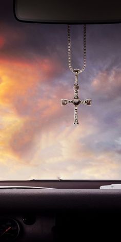 a car dashboard with a cross hanging from it's dash board and clouds in the background