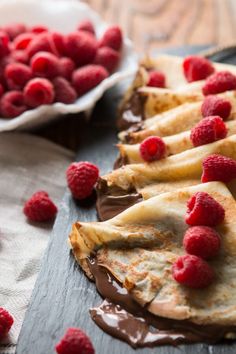 chocolate and raspberry crepes on a cutting board with fresh raspberries