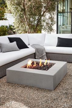 a fire pit sitting on top of a stone floor next to white couches and pillows