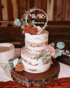 a three tiered wedding cake on top of a wooden slice with greenery and flowers