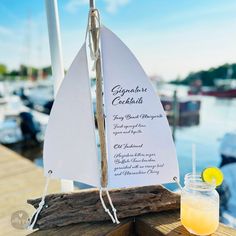 a drink sitting on top of a wooden table next to a boat in the water