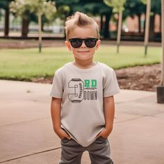 a young boy wearing sunglasses and standing in front of a park with his hands on his hips