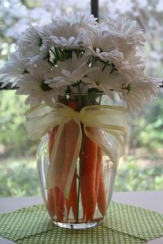 a vase filled with carrots and flowers on top of a green tablecloth covered table