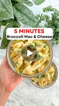 a hand holding a small bowl filled with broccoli macaroni and cheese