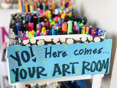 there is a sign that says you here comes your art room in front of many pens and pencils