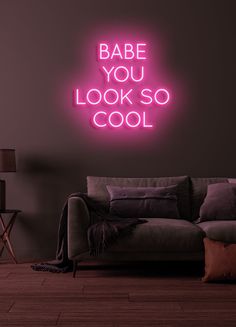 a neon sign that says babe you look so cool on the wall next to a couch