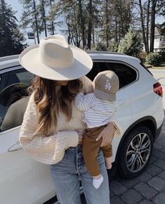 a woman holding a baby in her arms next to a white car with the door open