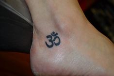 a small tattoo on the foot of a person with an omen symbol in black ink