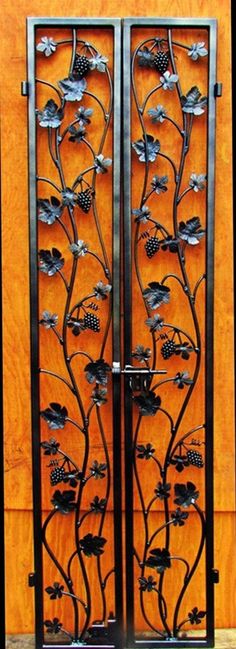 an iron gate with flowers and leaves on the sides, in front of a wooden wall