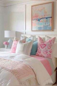 a white bed topped with lots of pillows next to a painting on the wall above it