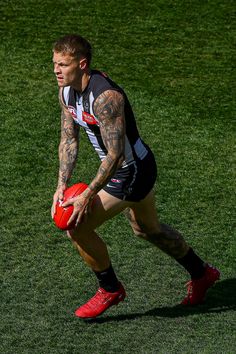 a tattooed man holding a red ball on top of a lush green field with grass