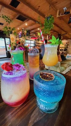 four different colored drinks sitting on top of a wooden table