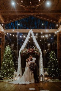 a bride and groom kissing in front of christmas trees at their winter wedding ceremony venue