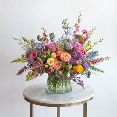 a vase filled with lots of colorful flowers on top of a marble topped side table