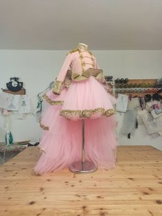 a mannequin dressed in pink and gold is standing on a wooden floor next to clothes