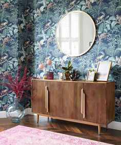 a living room with blue wallpaper and wooden cabinet in front of a round mirror