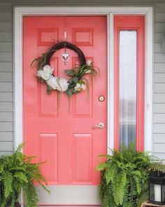 a pink door with a wreath on it and two potted plants next to it