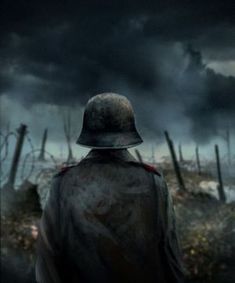 a man with a hat standing in the middle of a field under a cloudy sky