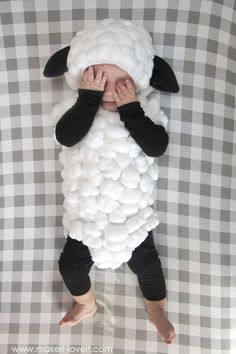 a baby in a sheep costume laying on top of a bed with his hands under his face