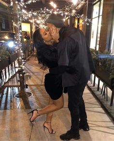 a man kissing a woman on the cheek in front of a building with christmas lights