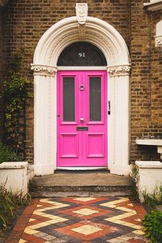 a bright pink door sits in front of a brick building with white trim and arched doorway