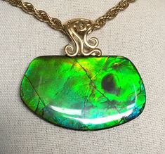 "This Ammolite pendant has a large green gem with golden overtones.  It has a shiny resin coating and measures in at 53mm x 31mm and hangs from a decorative sterling silver bail with gold wash (vermeil),  This gem has either a reverse horn or a bite mark.  Reverse horns show when the ammolite is split from the concretions, and sometime one gets a positive and negative gem surface.  When it is a negative surface, the horn will be reversed.  Bite marks often show loss of gem or a fractured gem area, so likely this is a reverse horn.  At very extreme angles some blue shows, as seen in the third photo.  It comes on an 18\" gold plated chain as shown.  Other lengths may be available on request.  Please remember that I offer combined shipping." Green Oval High Luster Jewelry, High Luster Green Jewelry For Gift, Green High Luster Jewelry For Gift, Bite Mark, Green Gem, The Horn, Green Gems, Resin Coating, Gold Wash