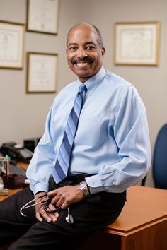 a man sitting on top of a wooden desk wearing a blue shirt and tie