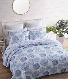 a bed with blue and white comforters in a room next to a potted plant