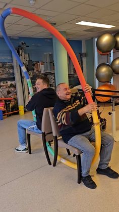 two men sitting on a bench in an office with balloons and streamers hanging from the ceiling