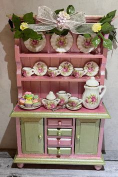 a pink and green china cabinet filled with tea cups, saucers and other items